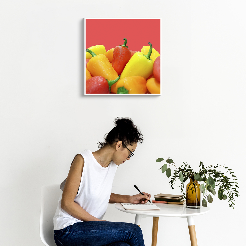 Foto su tela con peperoni colorati su sfondo rosso, appesa a una parete bianca sopra un tavolino