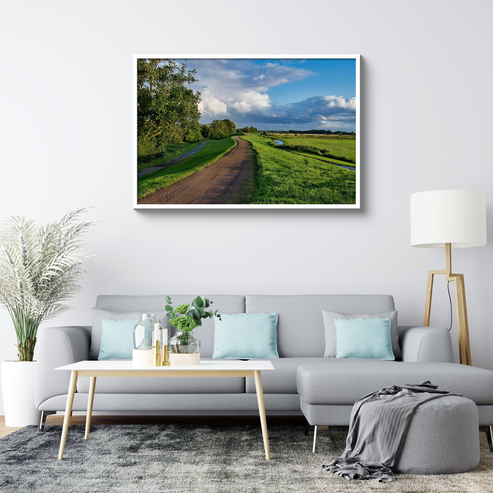 Landschaftsfoto hinter Acrylglas mit weissem Rahmen über einem grauen Sofa im hellen Wohnzimmer