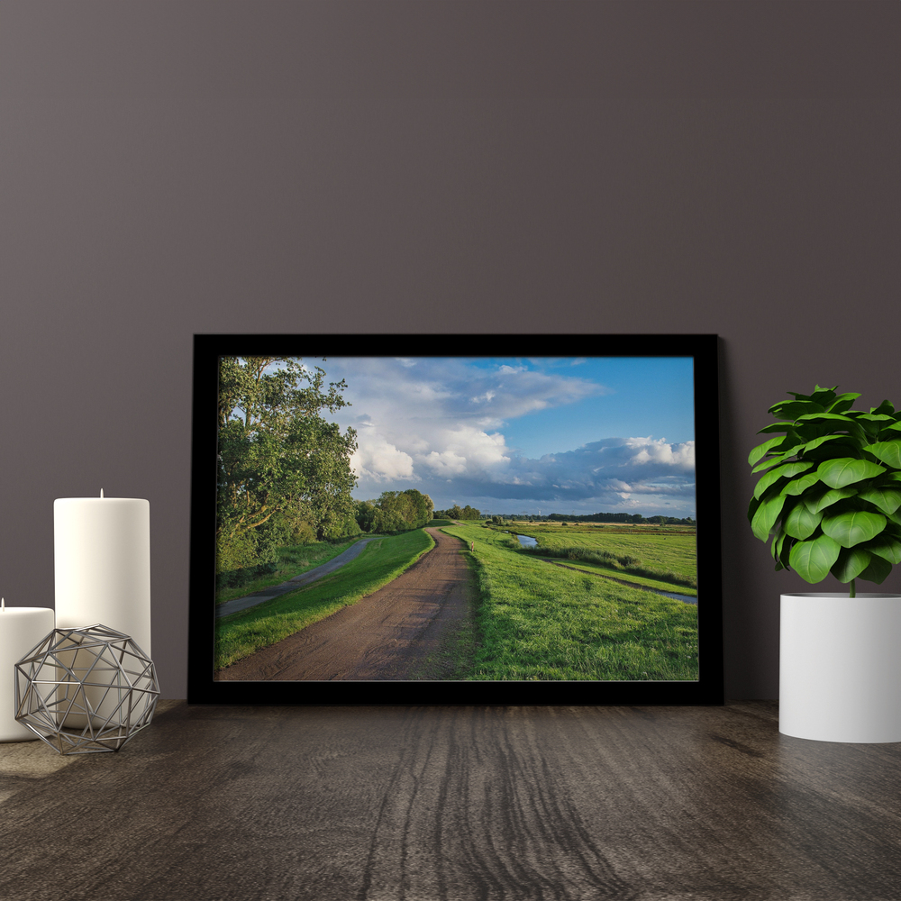 Landschaftsfoto hinter Acrylglas im schwarzen Rahmen auf einer Holzfläche neben Kerzen und einer Pflanze