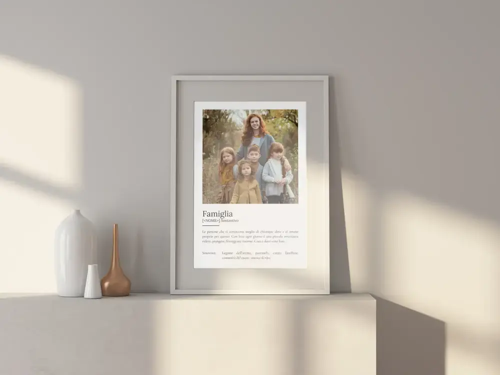 Poster con foto e definizione di famiglia in stile dizionario, in cornice chiara su una credenza accanto a due vasi