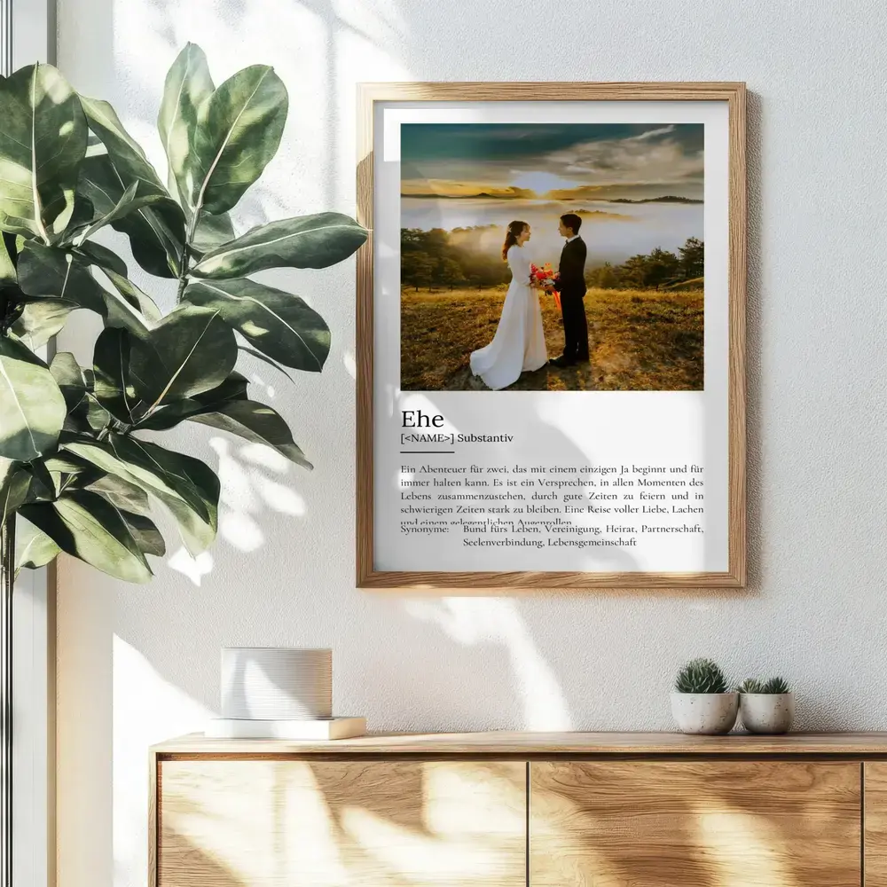 Definitionsposter zur Ehe mit grossem Hochzeitsfoto im Holzrahmen an der Wand über einer Kommode neben einer Pflanze