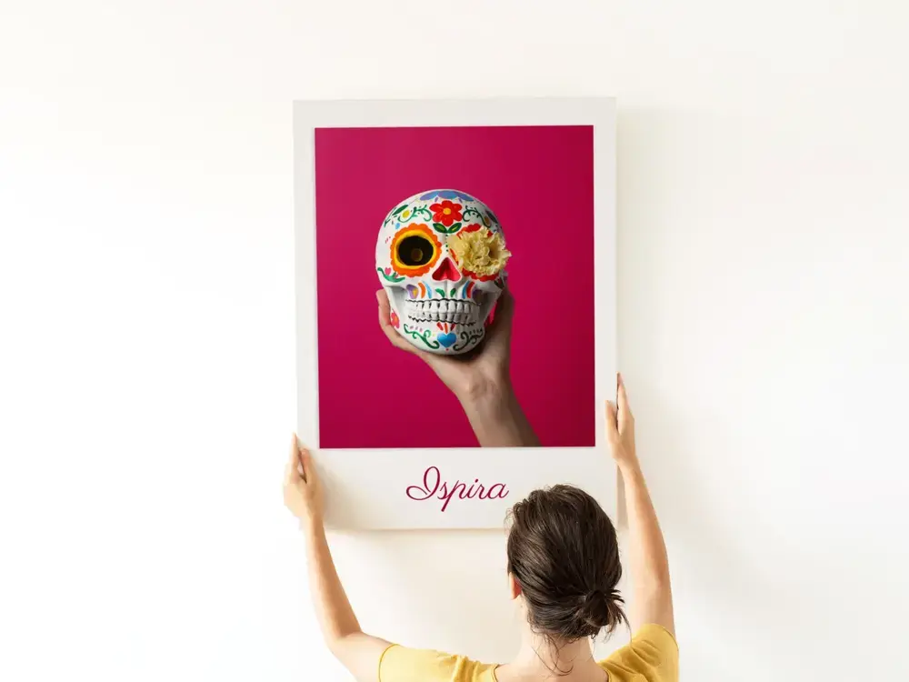 Poster personalizzato con teschio variopinto su sfondo rosa e scritta in corsivo, su una parete bianca