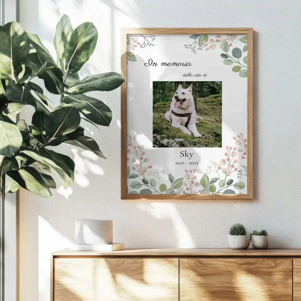 Poster in memoria di un cane con foto e fiori, in cornice di legno alla parete sopra una madia, accanto a una pianta
