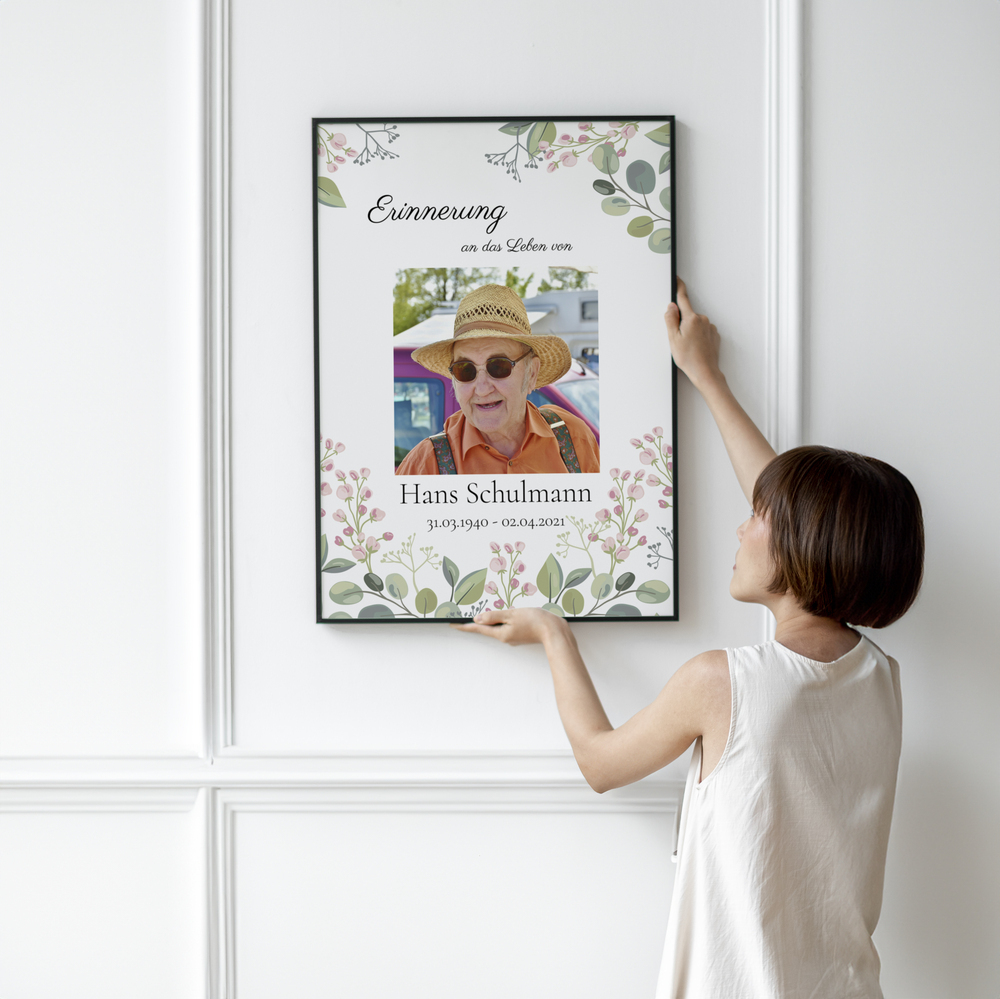 Trauerfoto mit Porträt und Blumenmotiv im schwarzen Rahmen an einer weissen Wand mit Zierleisten