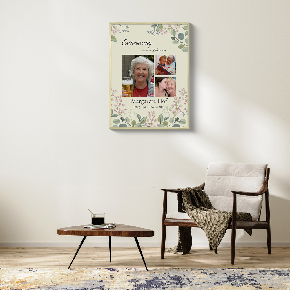 Trauercollage auf Leinwand mit drei Fotos und Blumenmotiv an heller Wohnzimmerwand neben einem Sessel